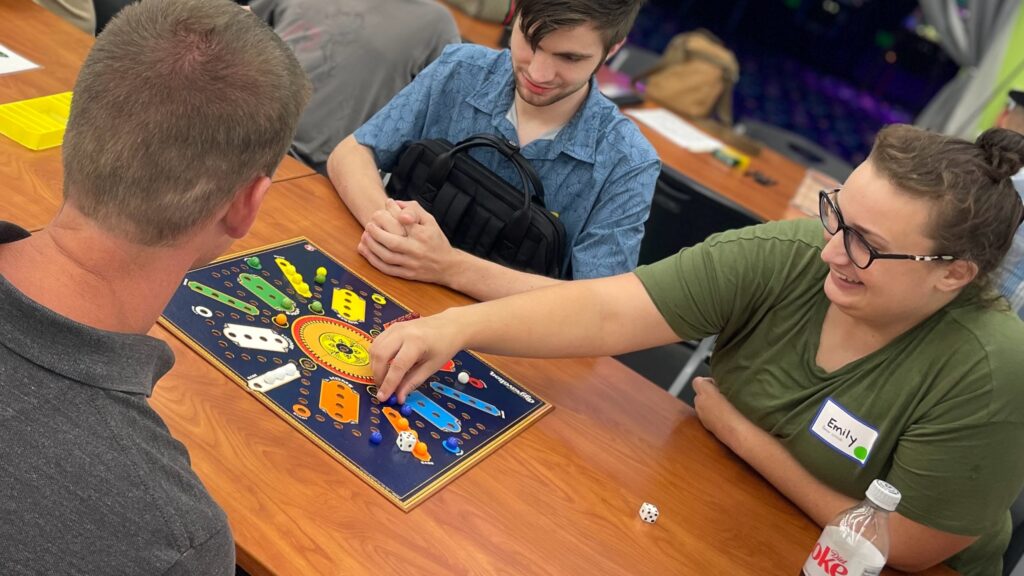 a woman and two men playing the game Aggravation.
